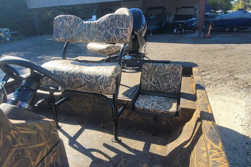 Slide: The Image of 2026 G3 Bay 21 GX Tunnel boat with camo seats and steering wheel, parked outdoors. - 21