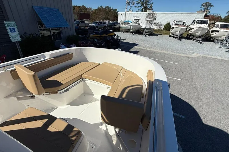 Slide: The Image of 2026 Bayliner Trophy T22CC boat with tan seating, parked outdoors near other boats. - 8