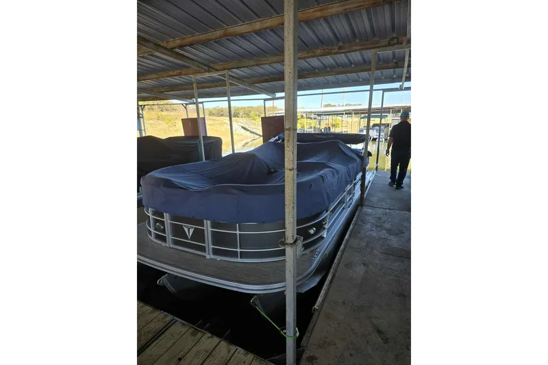 Slide: The Image of Covered 2023 Trifecta 24 RFE pontoon boat docked under a metal roof. - 1