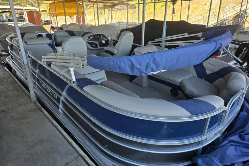 Slide: The Image of 2023 Trifecta 24 RFE pontoon boat with blue and gray seating, docked in a covered marina. - 4
