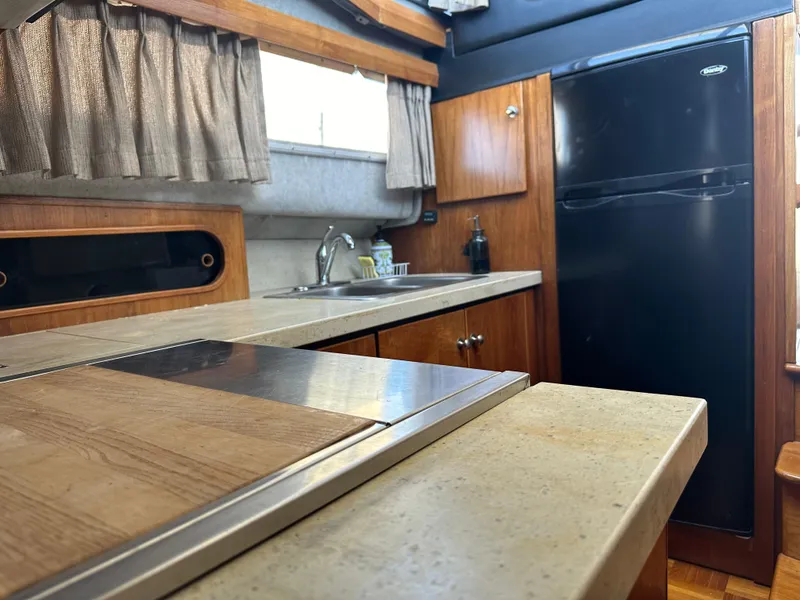Slide: The Image of 1987 Bayliner 3888 Motoryacht kitchen with wood cabinetry, countertop, and black refrigerator. - 12