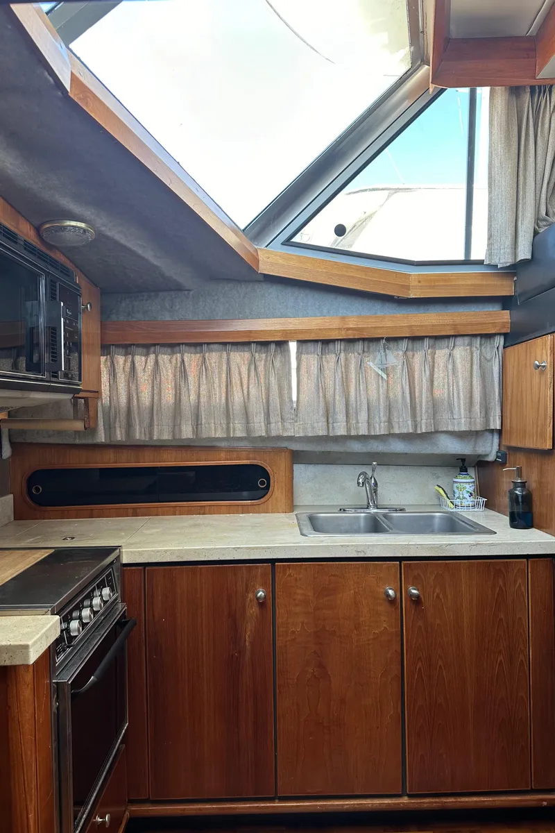 Slide: The Image of 1987 Bayliner 3888 Motoryacht kitchen with wood cabinets, stove, and sink under skylight. - 26