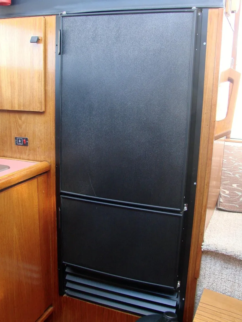Slide: The Image of 1987 Bayliner 3888 Motoryacht interior with black refrigerator and wooden cabinetry. - 6