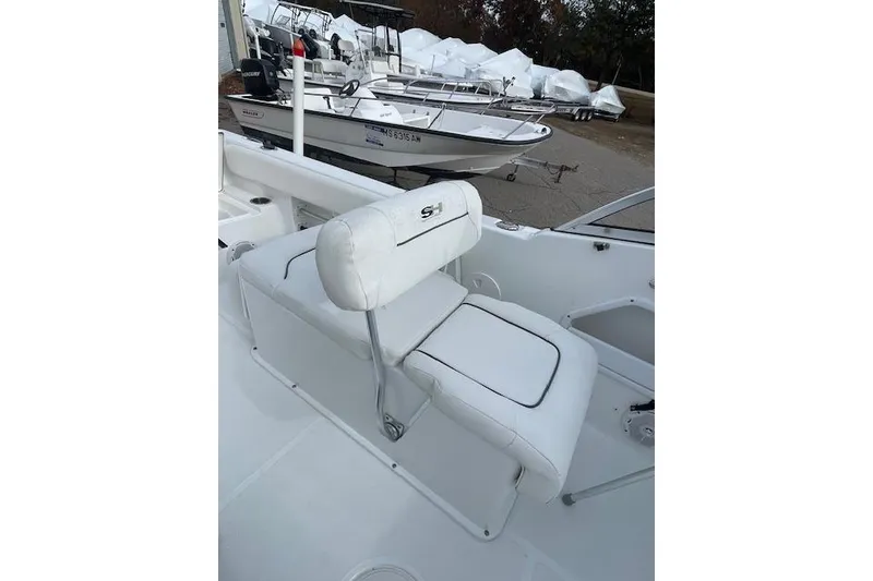 Slide: The Image of 2016 Seahunt 235 Escape DC boat interior with white seating and nearby docked boats. - 18