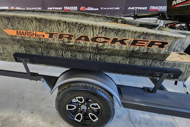 Slide: The Image of 2026 Tracker Grizzly 1756 T Marsh boat on trailer, camo design, displayed indoors. - 10