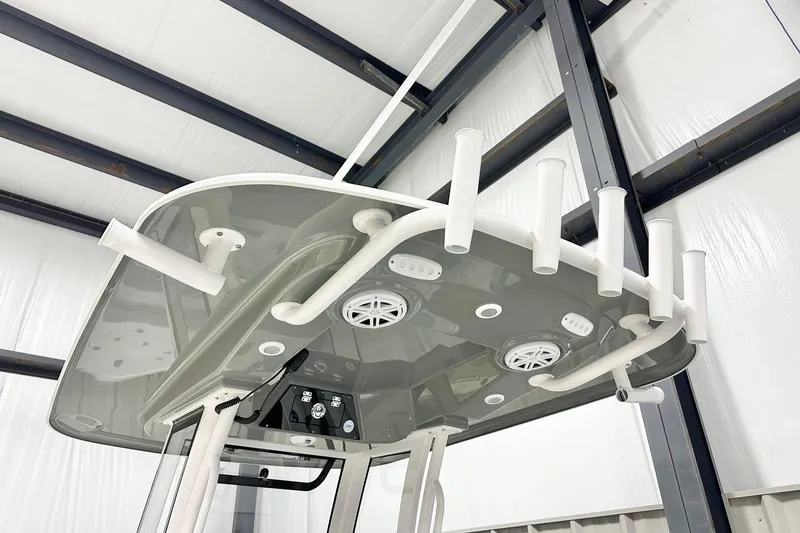 Slide: The Image of 2026 Sportsman Masters 247OE Bay Boat T-top with rod holders and speakers in a warehouse. - 7