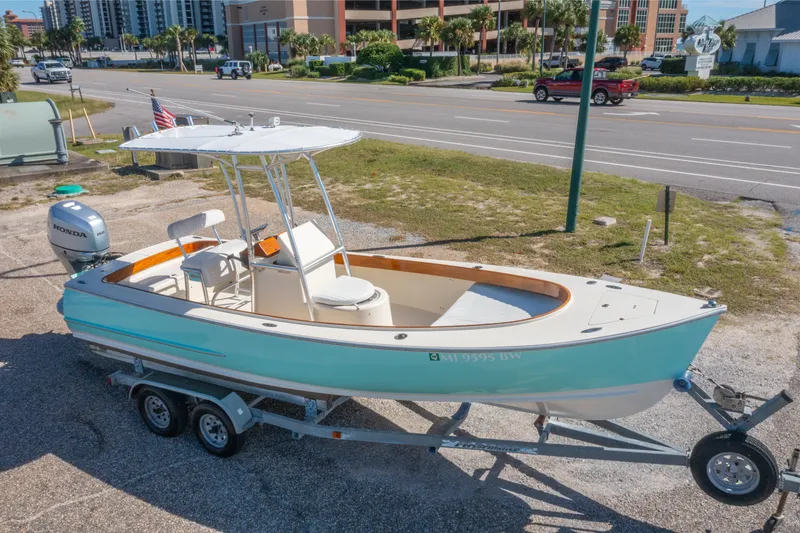 Slide: The Image of 2005 Oyster Bay 23 boat on trailer, parked near a road with buildings in the background. - 2