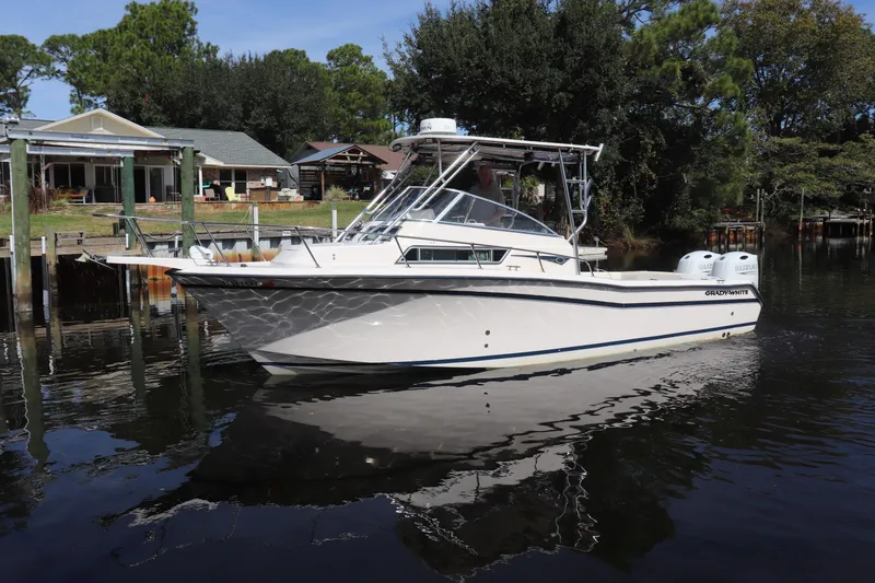 Slide: The Image of 1999 Grady-White Islander 268 boat docked on calm water, surrounded by trees and houses. - 56