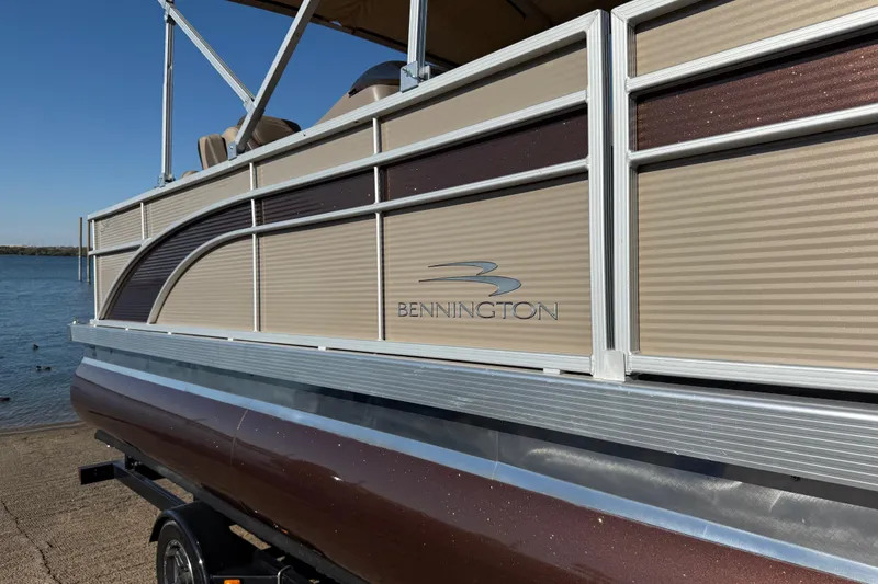 Slide: The Image of 2020 Bennington 21SF pontoon boat by the water, showcasing sleek design and metallic finish. - 87