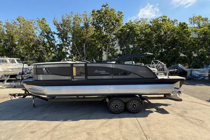 Slide: The Image of 2026 Barletta Lusso 23UC pontoon boat on trailer, parked outdoors with trees in background. - 117