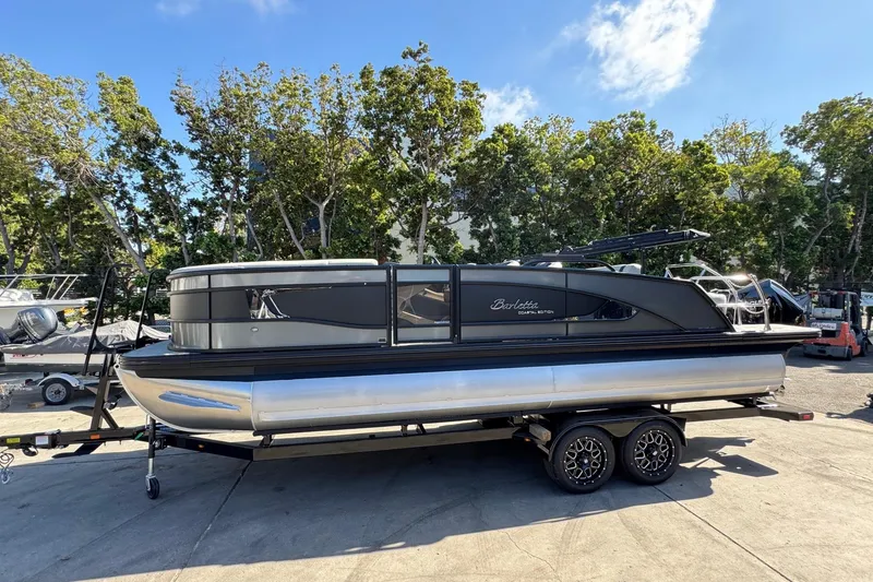 Slide: The Image of 2026 Barletta Lusso 23UC pontoon boat on trailer, parked outdoors with trees in background. - 118