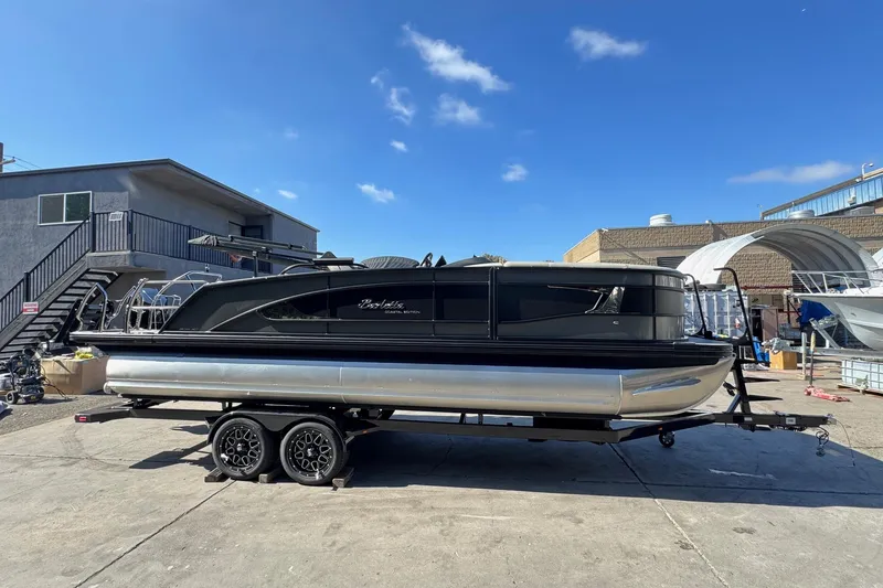 Slide: The Image of 2026 Barletta Lusso 23UC pontoon boat on trailer, parked outdoors under clear blue sky. - 125