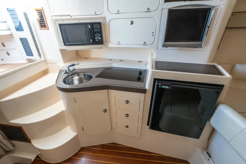 Slide: The Image of 2005 Grady-White Express 330 boat interior with kitchenette, sink, microwave, and compact fridge. - 28