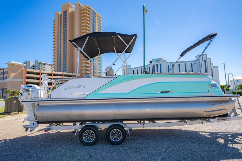 Slide: The Image of 2021 Silver Wave 2410 SW5 JS pontoon boat on trailer, urban backdrop. - 5