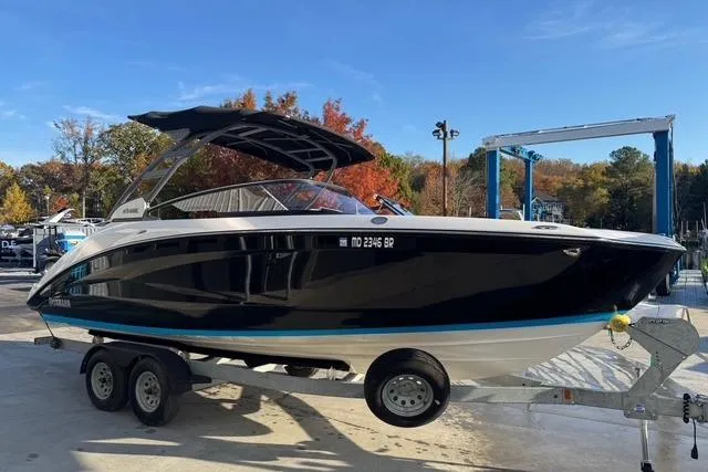 The Image of 2021 Yamaha Boats 252SE on trailer, black hull, outdoor setting, autumn trees in background. - 2