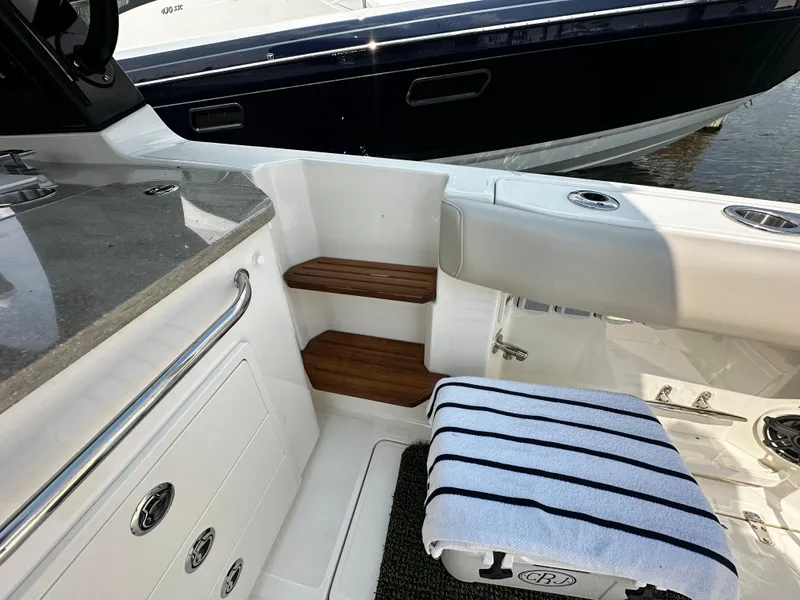 Slide: The Image of 2022 Boston Whaler 350 Realm interior with seating, wooden steps, and striped towel. - 13