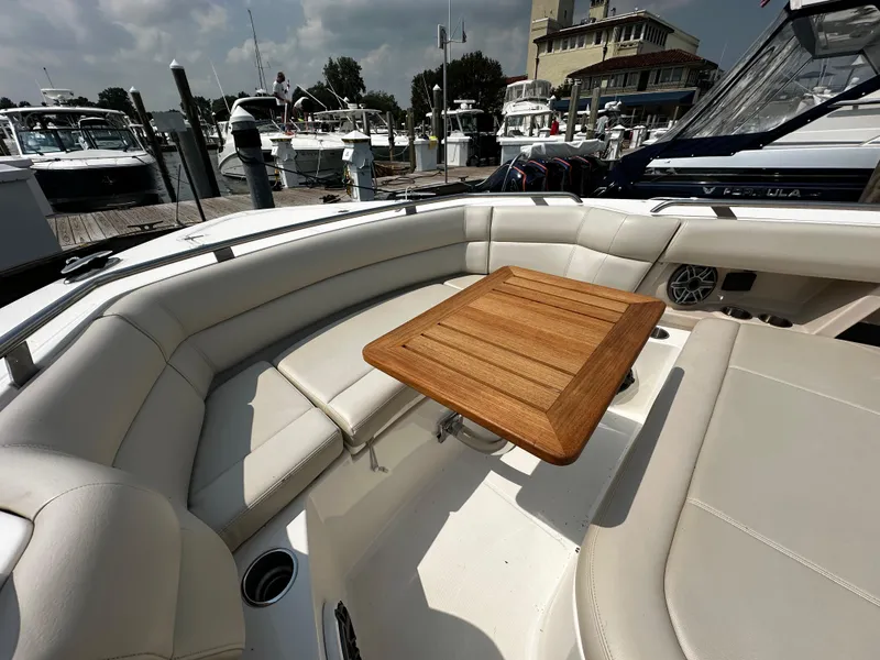 Slide: The Image of 2022 Boston Whaler 350 Realm boat interior with cushioned seating and wooden table at marina. - 28