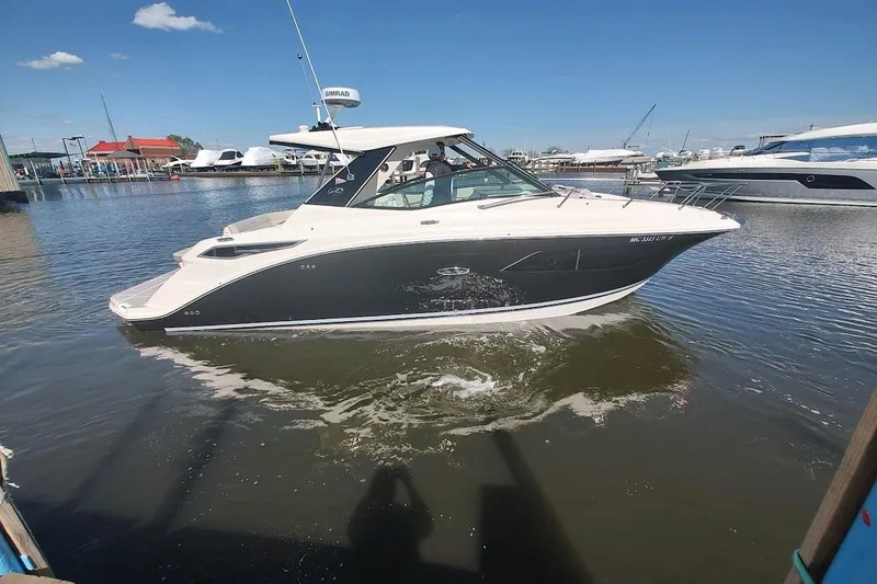 Slide: The Image of 2023 Sea Ray 320 Sundancer cruising in a marina under a clear blue sky. - 0