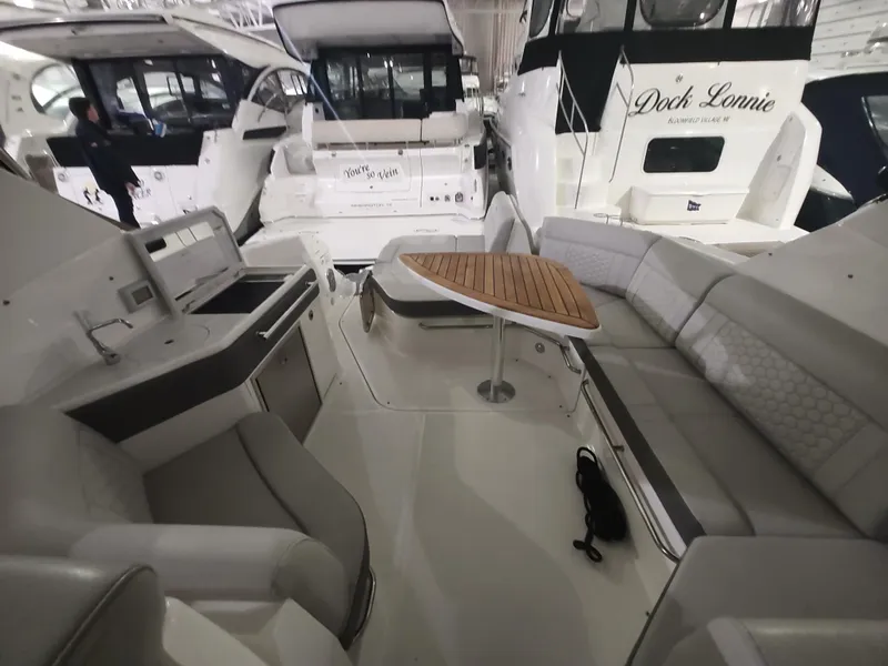 Slide: The Image of 2023 Sea Ray 320 Sundancer interior with seating and table in a marina. - 12