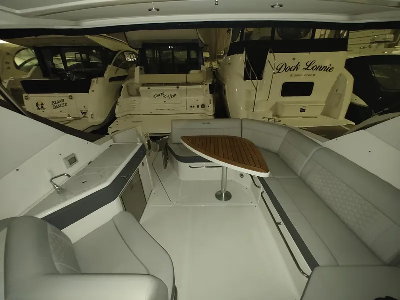 Slide: The Image of 2023 Sea Ray 320 Sundancer interior with seating and table, docked among other boats. - 21