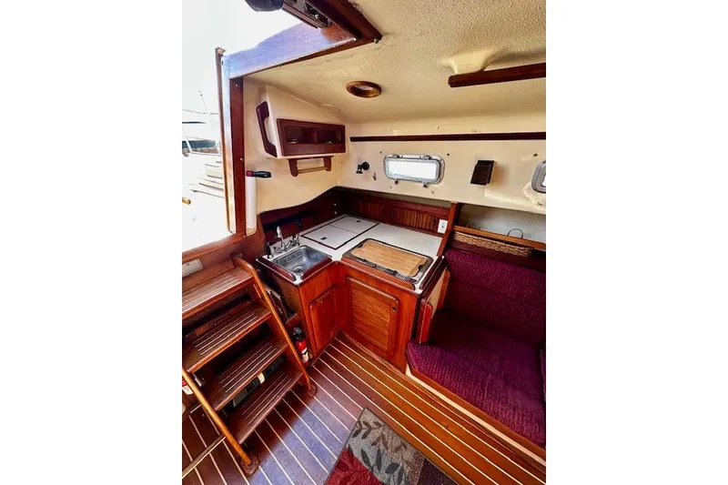 Slide: The Image of 1987 Island Packet 27 interior with wooden cabinetry, compact kitchen, and seating area. - 12