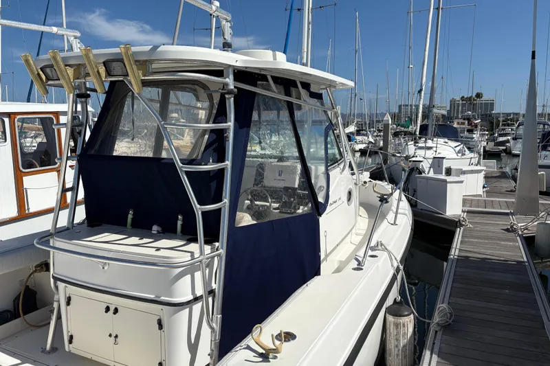 Slide: The Image of 2003 Boston Whaler 290 Outrage docked at marina, featuring blue canopy and fishing rod holders. - 3