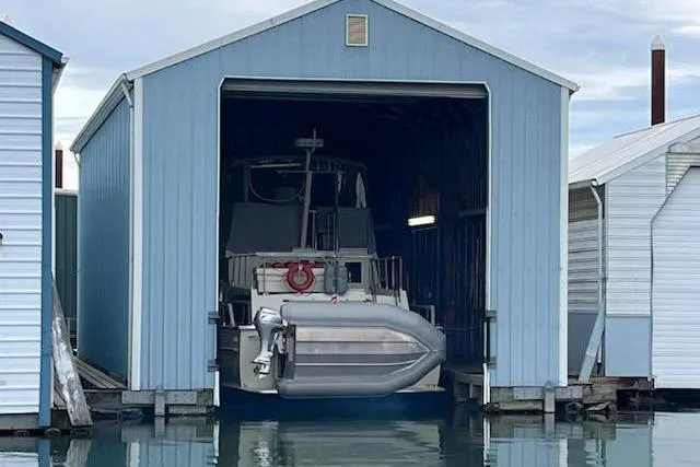 Slide: The Image of Custom 1980 boathouse with boat inside, blue exterior, docked on calm water. - 4