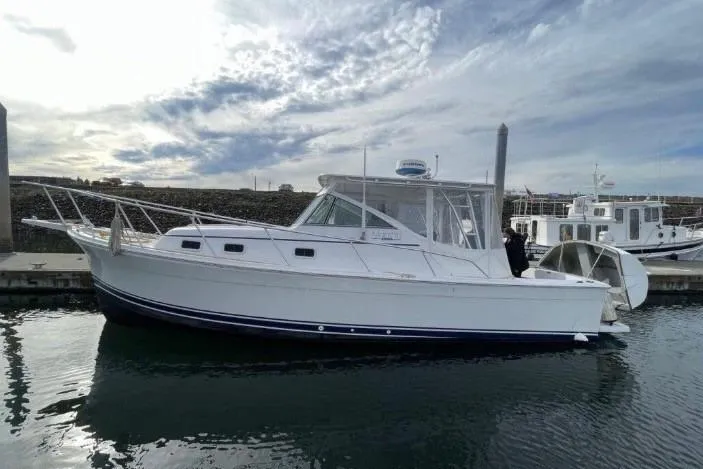 The Image of 1998 Mainship Pilot 30 boat docked in a marina under a cloudy sky. - 0