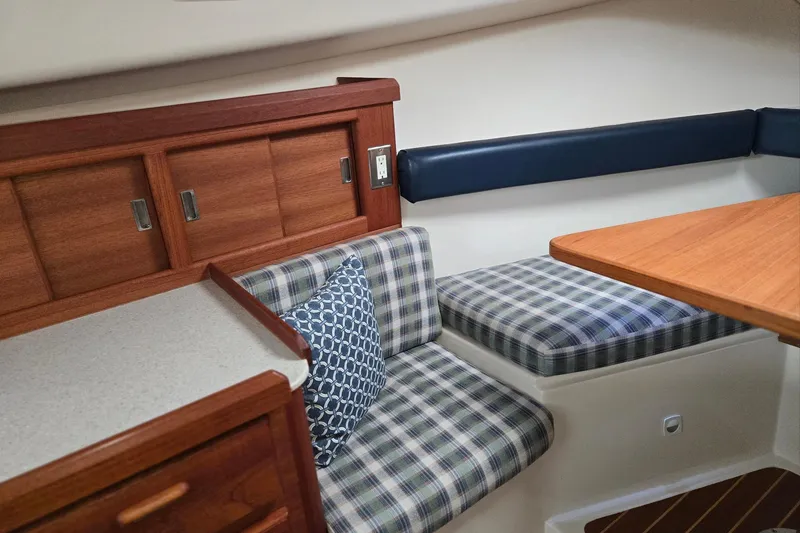 Slide: The Image of 1998 Mainship Pilot 30 interior with plaid seating, wooden cabinetry, and a cozy dining area. - 59