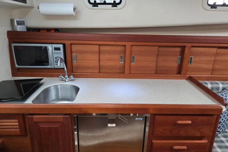 Slide: The Image of 1998 Mainship Pilot 30 galley with microwave, sink, and wooden cabinetry. - 64
