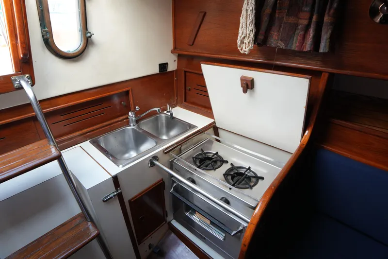 Slide: The Image of 1983 Cape Dory 30c yacht galley with stove, sink, and wooden cabinetry. - 28