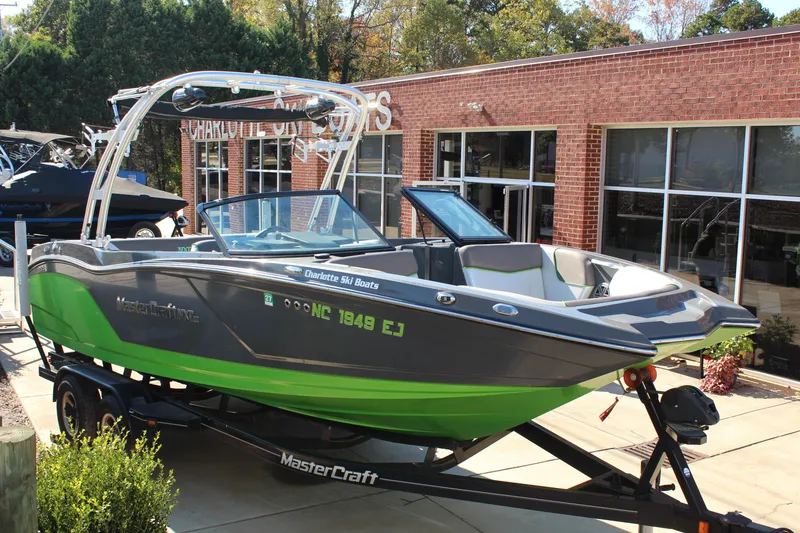 The Image of 2017 MasterCraft NXT22 boat in green and gray on a trailer outside a brick building. - 1