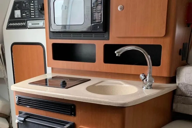 Slide: The Image of 2006 Crownline 250 CR boat interior kitchen with sink, stove, and microwave. - 7