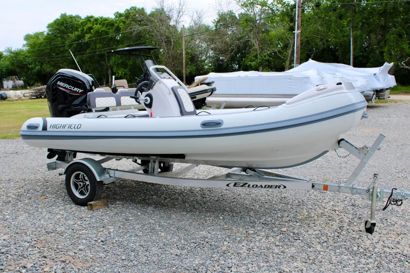 Slide: The Image of 2024 Highfield Sport 460 boat on trailer, featuring a Mercury engine, parked outdoors. - 12