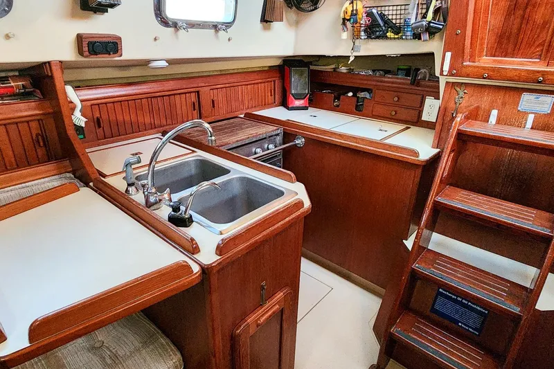 Slide: The Image of Interior of a 1990 Island Packet 32 sailboat, featuring a compact wooden kitchen area. - 27
