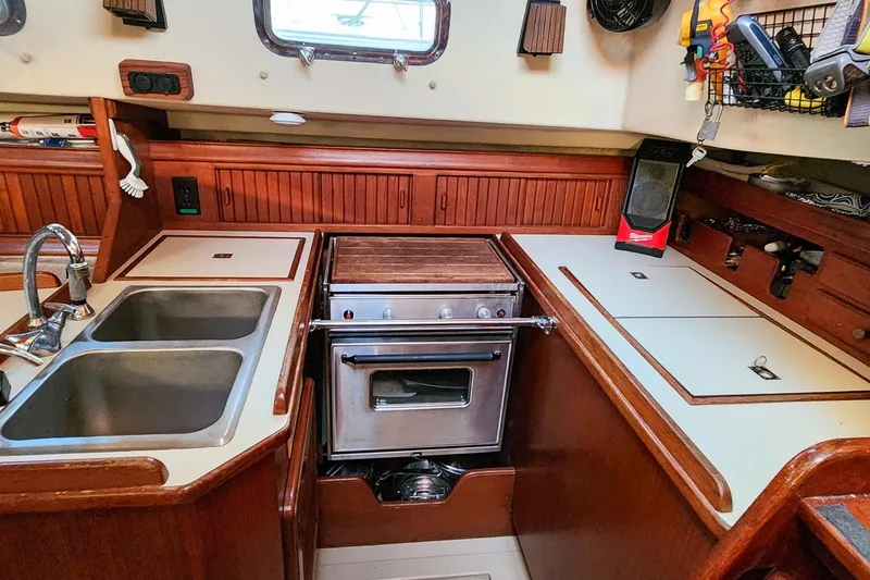 Slide: The Image of 1990 Island Packet 32 yacht kitchen with dual sinks, stove, and wooden cabinetry. - 28