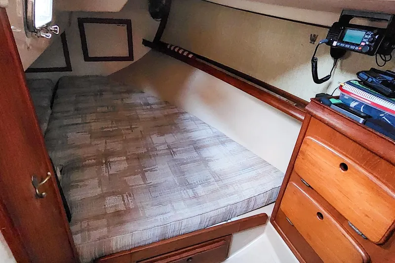 Slide: The Image of 1990 Island Packet 32 cabin interior with bed, wooden drawers, and radio equipment. - 45