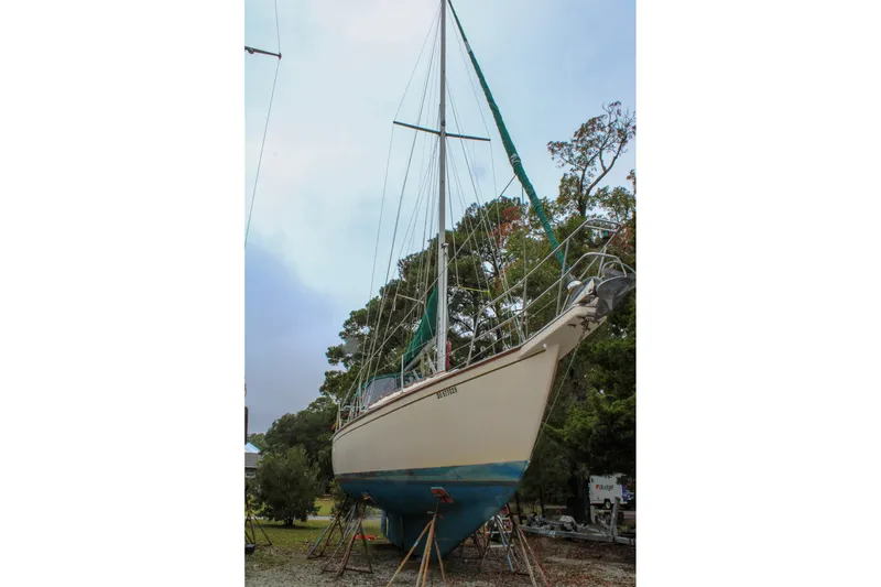 Slide: The Image of 1990 Island Packet 32 sailboat on stands, surrounded by trees, under a cloudy sky. - 50