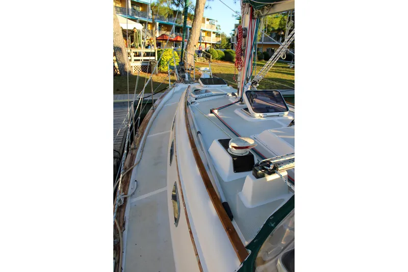 Slide: The Image of 1990 Island Packet 32 sailboat deck with rigging and hatches, docked near a resort. - 9