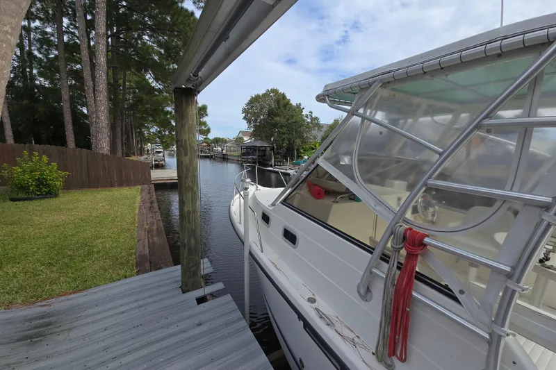 Slide: The Image of 2001 Shamrock 26 boat docked by a wooden pier, surrounded by trees and calm water. - 4