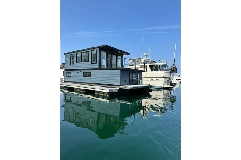 Slide: The Image of Modern 2026 East Coast Houseboat Bayview floating on calm water, docked beside a yacht. - 11