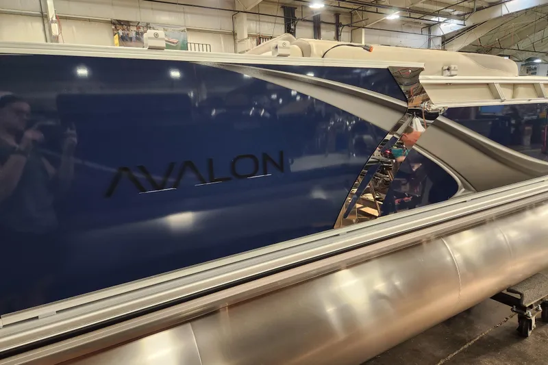 Slide: The Image of 2026 Avalon LSZ Quad Lounger pontoon boat in a showroom, featuring sleek blue design. - 10