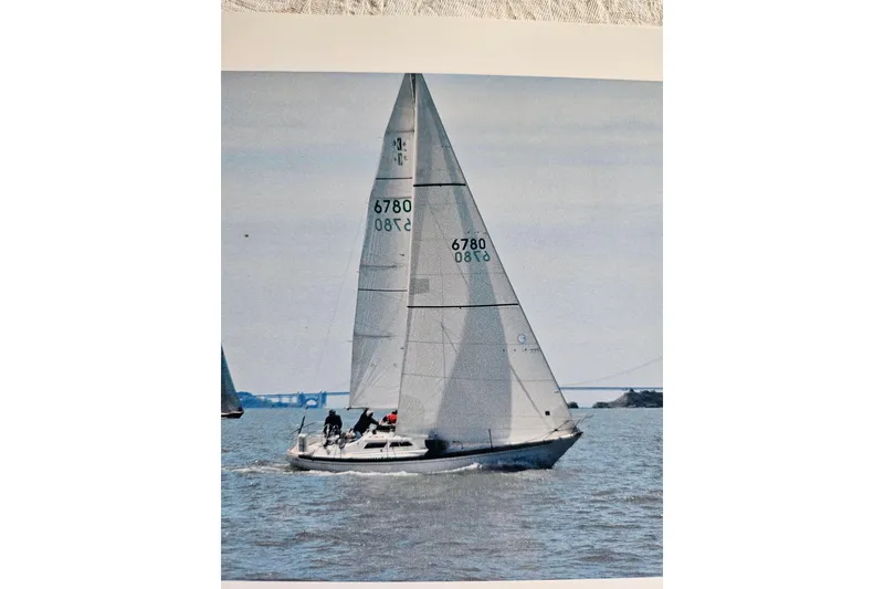 Slide: The Image of 1978 Islander 36 sailboat on open water, sails fully raised, with distant bridge view. - 1