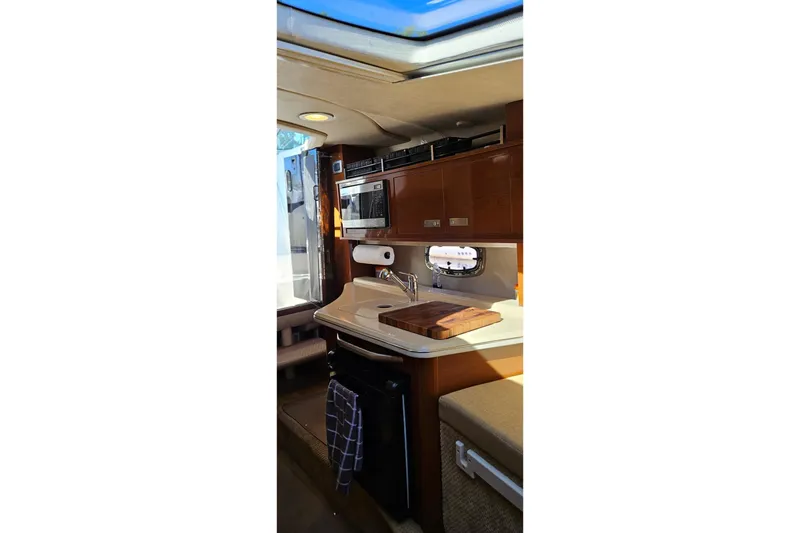 Slide: The Image of 2009 Sea Ray 270 Sundancer interior kitchen with sink, microwave, and wooden cabinetry. - 9