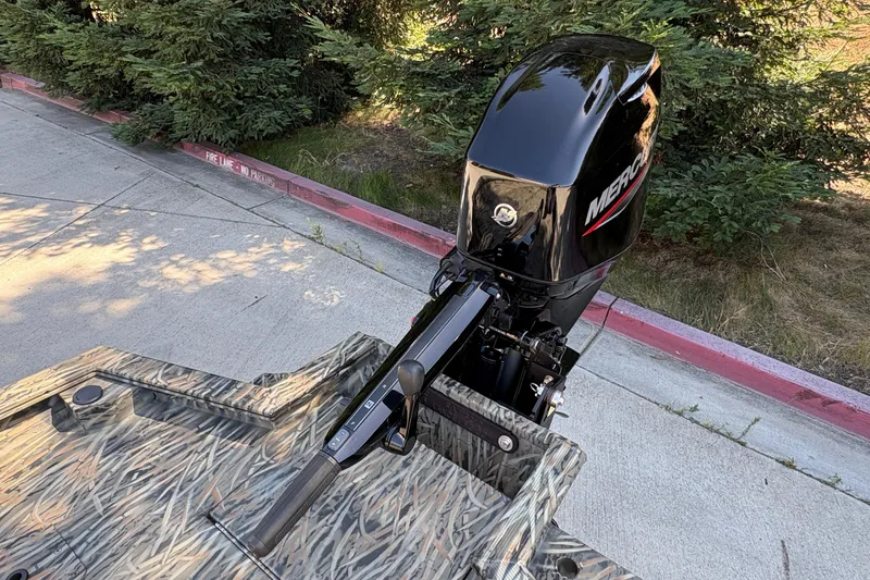 Slide: The Image of 2026 Tracker Grizzly 1650 T Prairie Wings Edition with Mercury outboard motor, parked near greenery. - 17