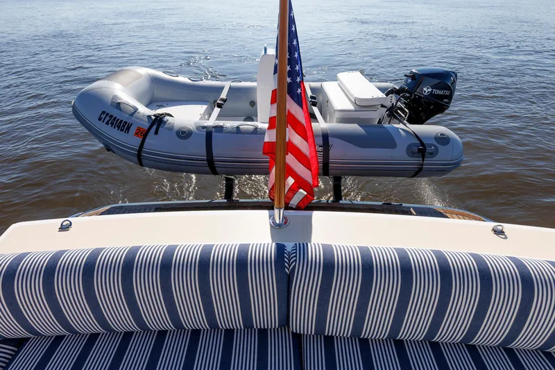 Slide: The Image of 2019 Grand Banks 44 Eastbay SX with striped seating, American flag, and inflatable boat on water. - 20