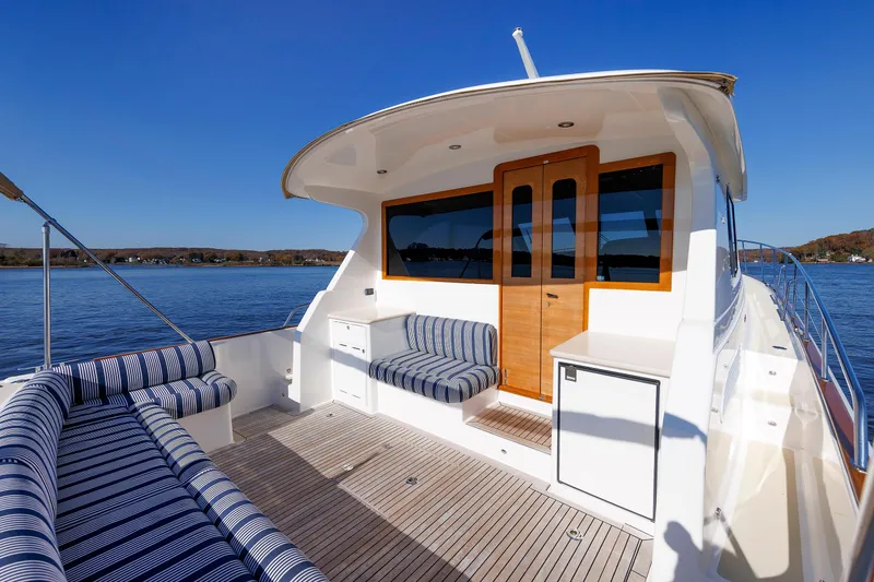 Slide: The Image of 2019 Grand Banks 44 Eastbay SX yacht with striped seating, wooden accents, and scenic water view. - 23