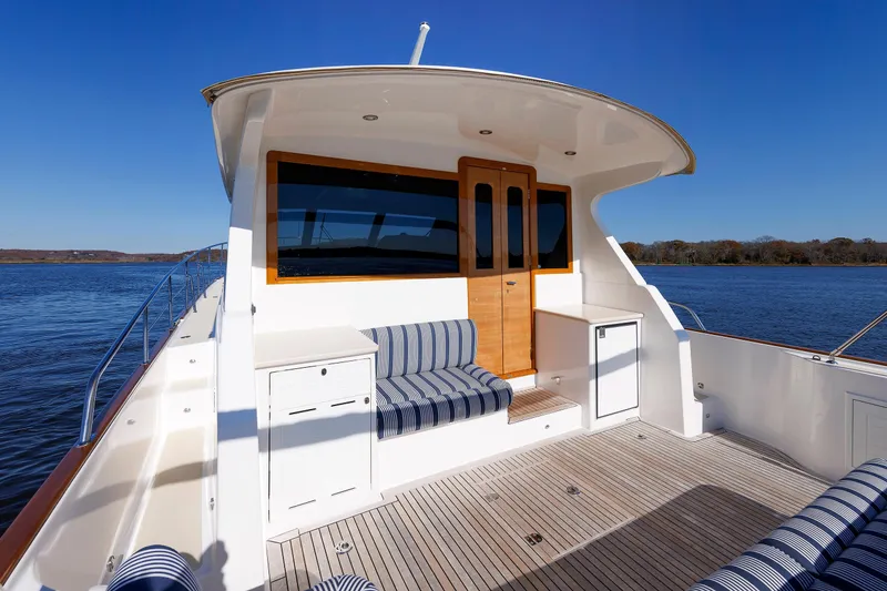Slide: The Image of 2019 Grand Banks 44 Eastbay SX yacht deck with striped seating, wooden door, and scenic water view. - 25