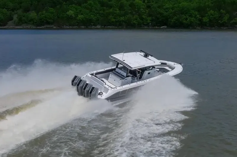 Slide: The Image of 2024 HCB 42 Lujo boat speeding on a lake with lush green shoreline. - 6