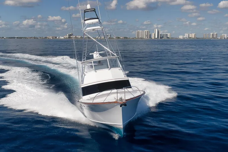 Slide: The Image of 1998 Rybovich Convertible yacht cruising on open water with city skyline in background. - 48